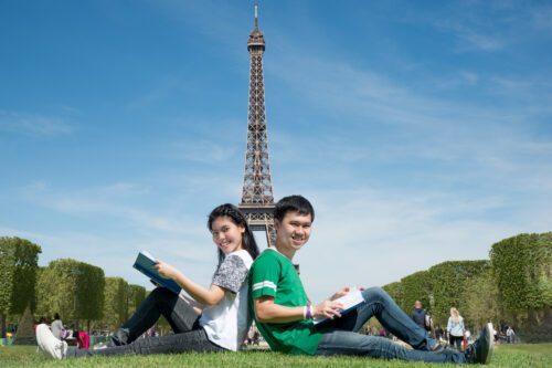 Two people sitting on the grass in front of a tower.